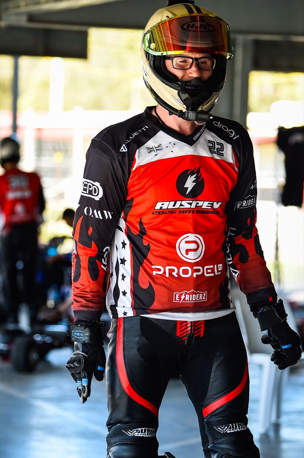 An ESRA racer in full gear and a gold helmet, smiling in the pits